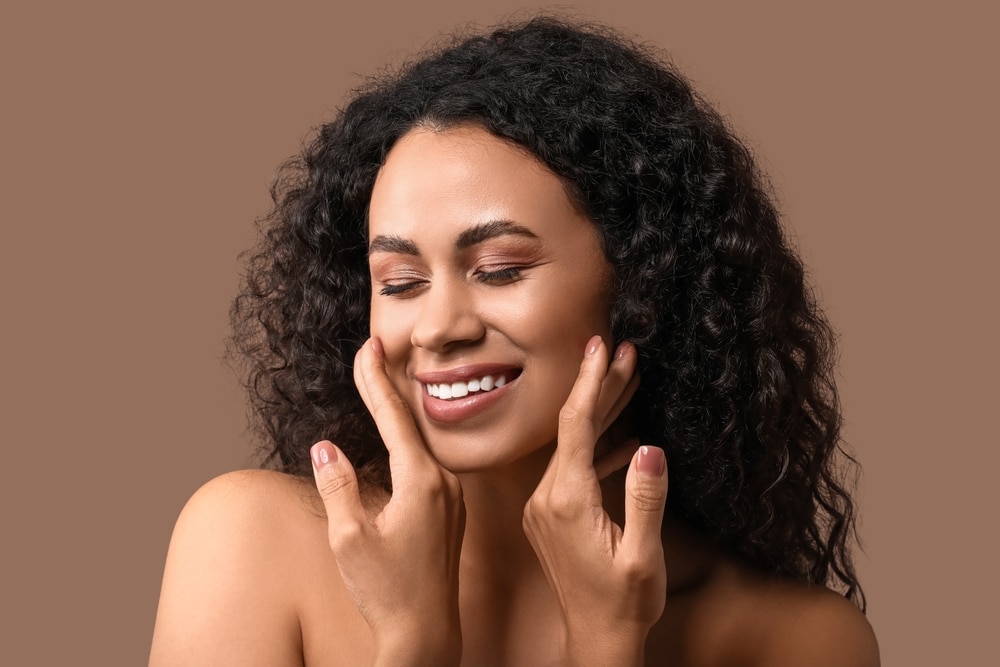 Beautiful young woman with radiant, healthy skin smiling against brown background, concept of natural beauty and skincare.